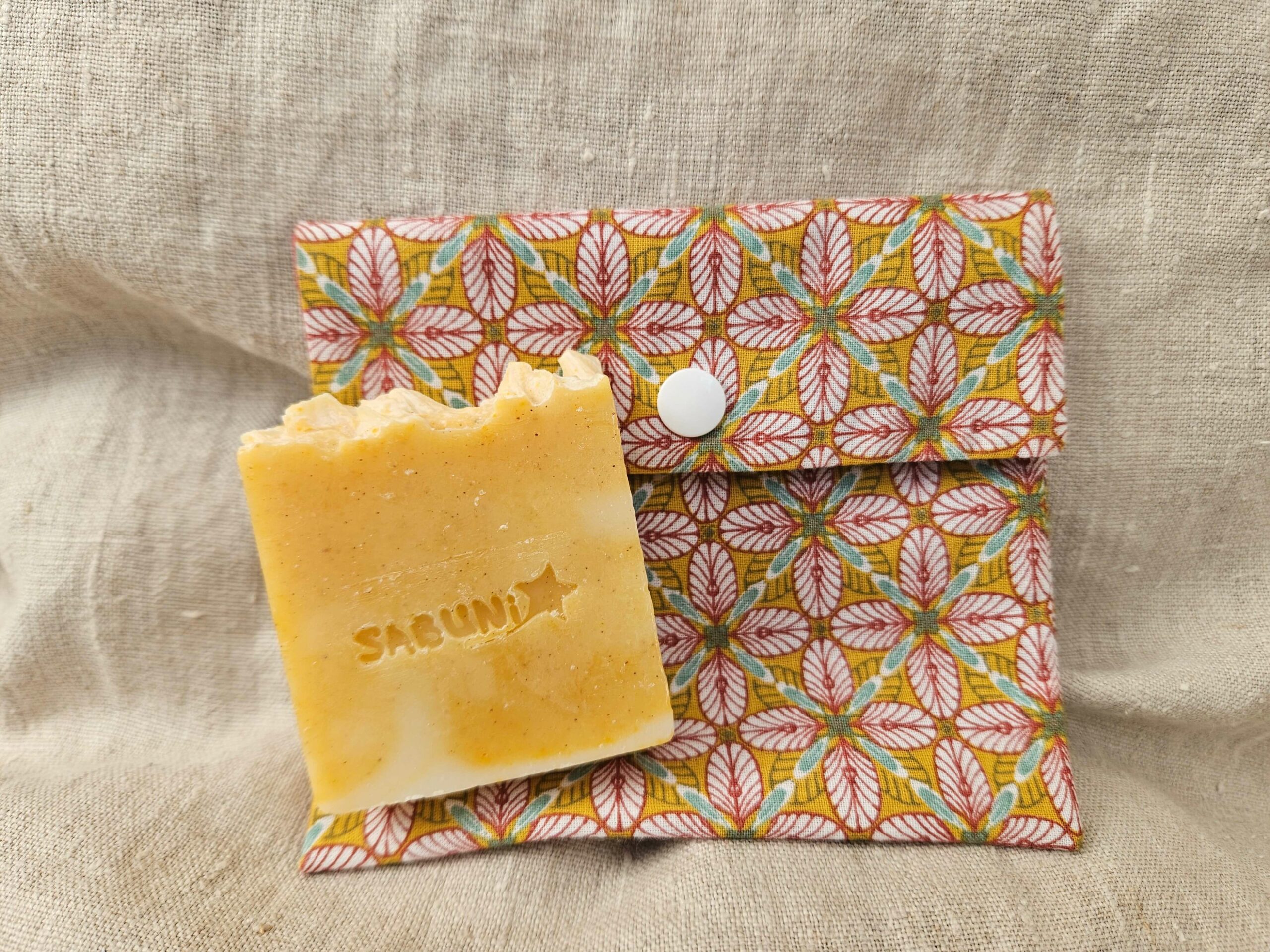 Accessoire zéro déchet de la savonnerie artisanale Sabuni & Cie. Pochette à savon artisanale, Tissu eoko-tex bio. Fait main dans les Yvelines. Pochette à savon sur fond en fibre naturelle.