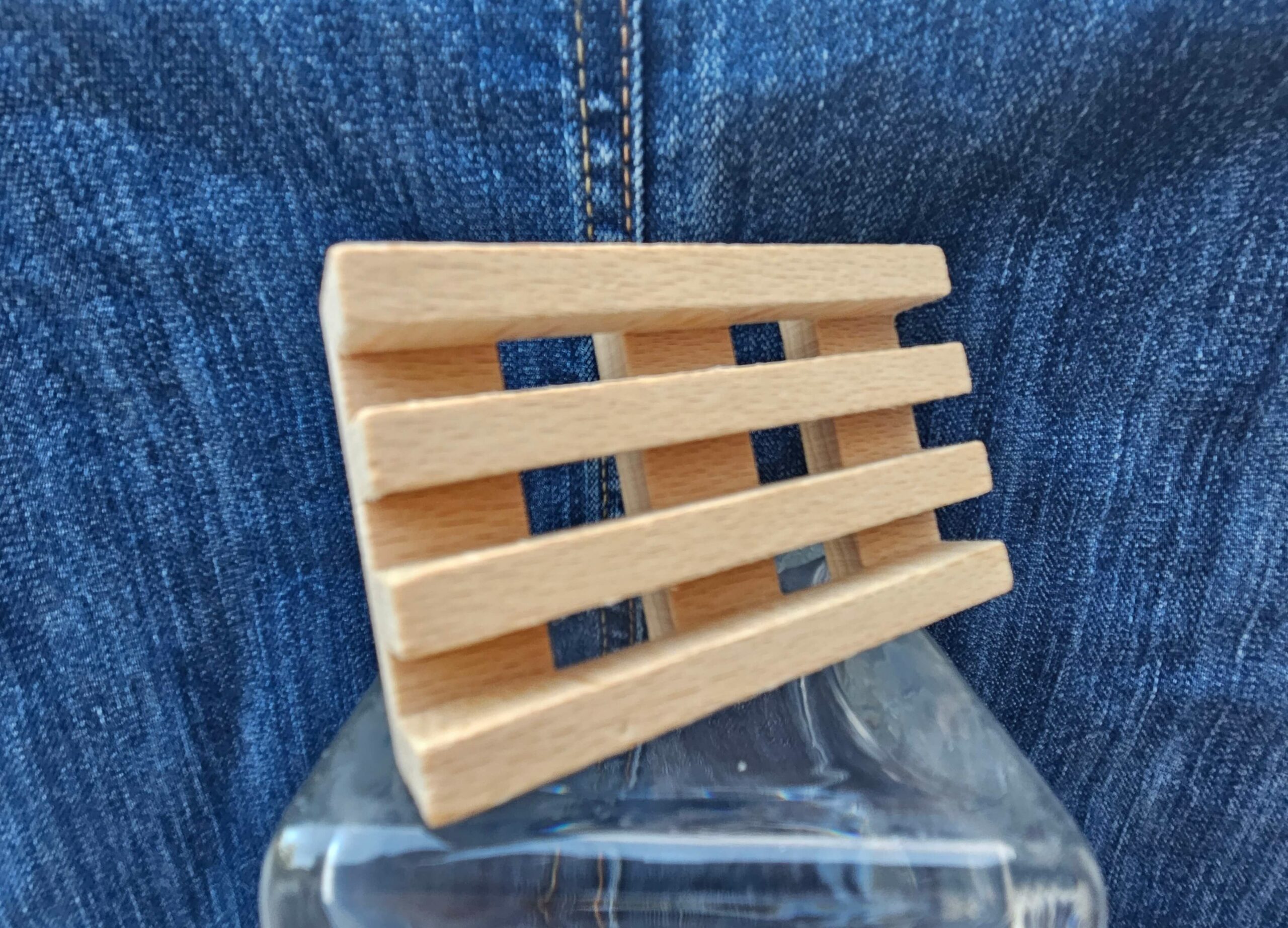 Accessoire zéro déchet de la savonnerie artisanale Sabuni & Cie. Porte savon artisanal en bois massif des Voges et d’Alsace. Porte savon en bois sur fond bleu jeans.