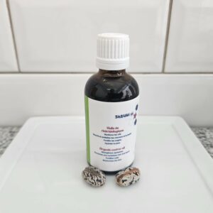 Huile de Ricin biologique, reconditionnée par la savonnerie artisanale Sabuni & Cie, dans un flacon en verre opaque, posé devant du carrelage style métro.