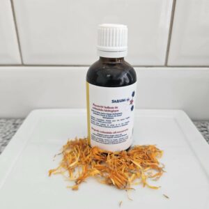 Macérat huileux de calendula précieux, fait à la main, par la savonnerie artisanale Sabuni & Cie, selon la recette ancestrale, dans un flacon en verre opaque, posé devant du carrelage style métro.